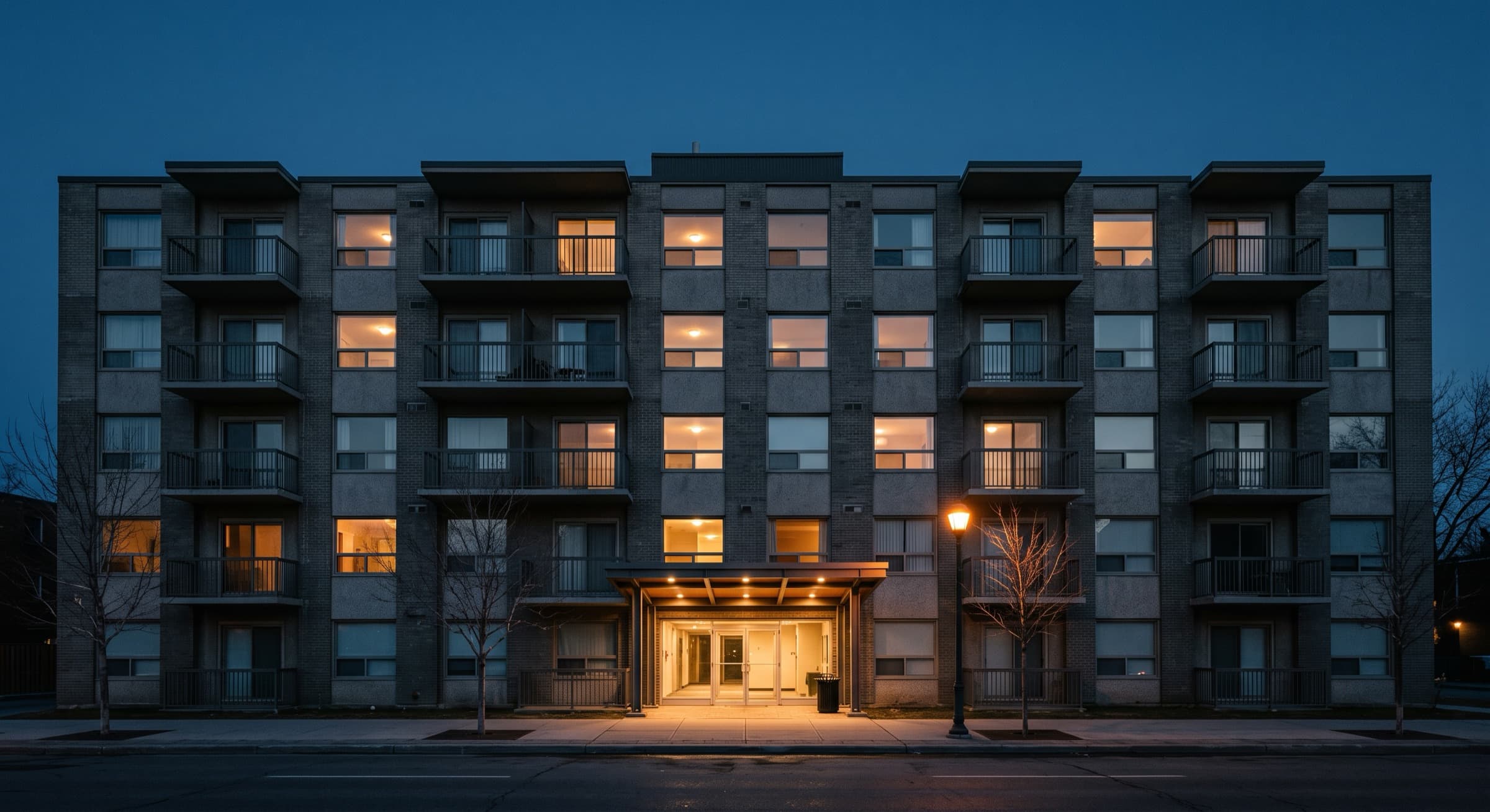A six storey apartment building at blue hour, its windows lit in an irregular pattern
